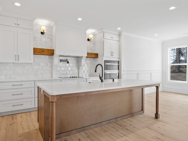 kitchen featuring white cabinetry, a breakfast bar area, ornamental molding, a kitchen island with sink, and black electric stovetop