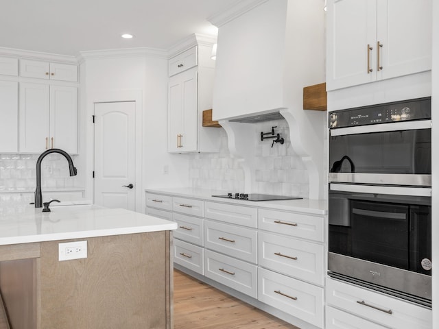 kitchen with light hardwood / wood-style flooring, white cabinetry, a kitchen island with sink, black electric stovetop, and stainless steel double oven