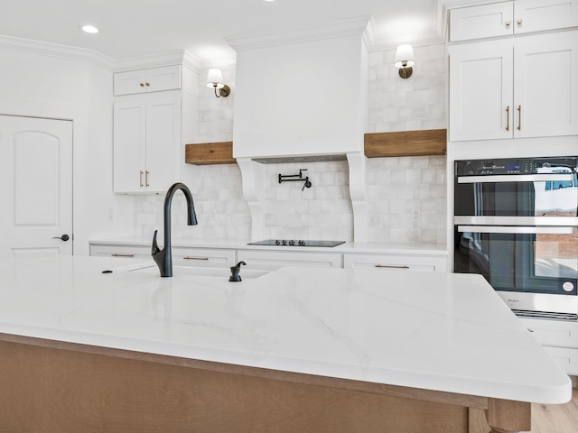 kitchen featuring stainless steel double oven, light stone countertops, and white cabinets