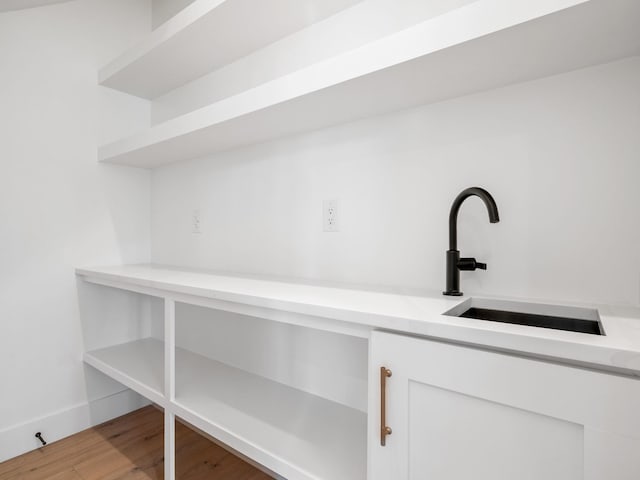 bar featuring sink, light hardwood / wood-style flooring, and white cabinets