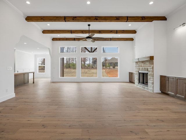 unfurnished living room with a stone fireplace, beam ceiling, and light hardwood / wood-style floors