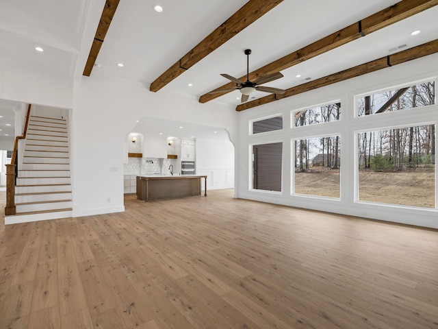 unfurnished living room with sink, beam ceiling, light hardwood / wood-style flooring, and ceiling fan