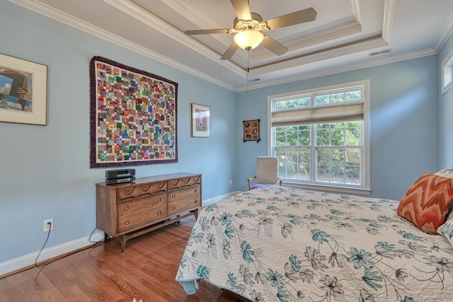 bedroom with ceiling fan, ornamental molding, wood-type flooring, and a raised ceiling