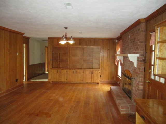 unfurnished living room featuring wooden walls, a chandelier, ornamental molding, light hardwood / wood-style floors, and a brick fireplace