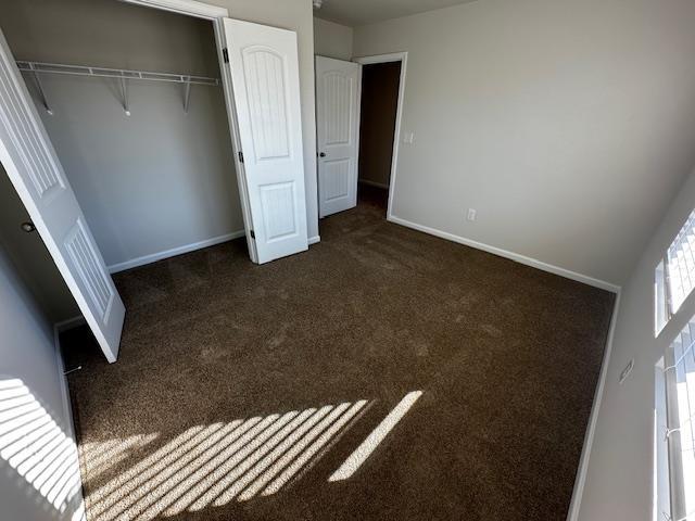 unfurnished bedroom with dark colored carpet and a closet