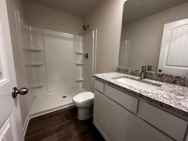 bathroom with toilet, hardwood / wood-style floors, vanity, and walk in shower