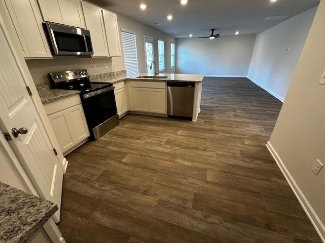 kitchen with sink, light stone counters, kitchen peninsula, stainless steel appliances, and white cabinets