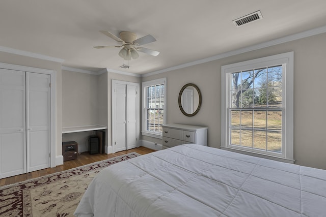 bedroom with crown molding, hardwood / wood-style floors, two closets, and ceiling fan