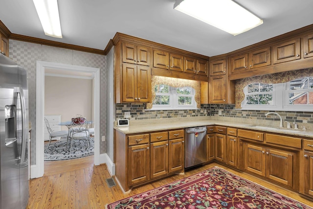 kitchen featuring sink, backsplash, ornamental molding, light hardwood / wood-style floors, and stainless steel appliances