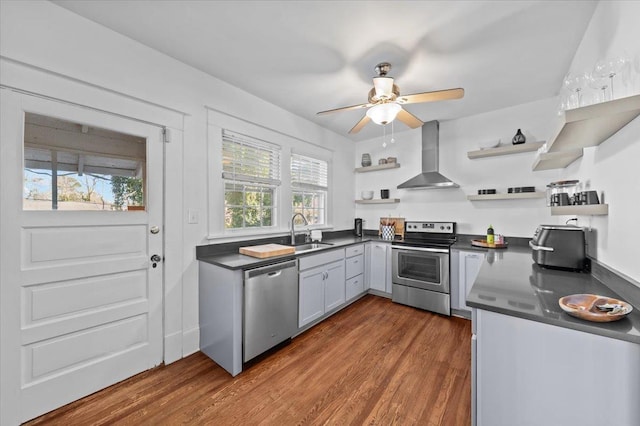 kitchen with sink, ceiling fan, stainless steel appliances, dark wood-type flooring, and wall chimney exhaust hood