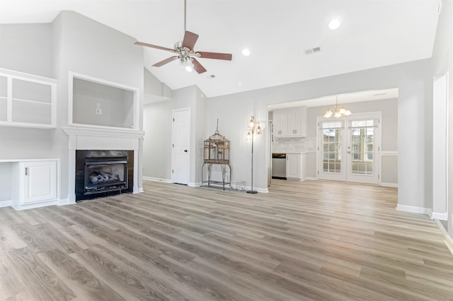 unfurnished living room featuring a tiled fireplace, high vaulted ceiling, ceiling fan with notable chandelier, and light hardwood / wood-style floors