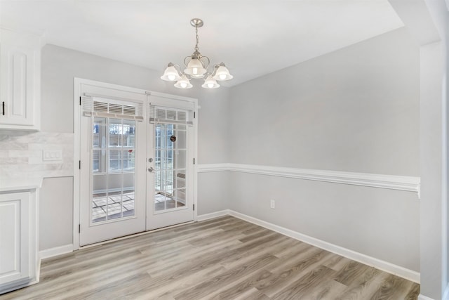 unfurnished dining area featuring a notable chandelier, light hardwood / wood-style flooring, and french doors