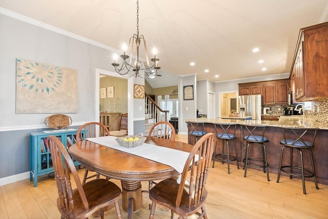 dining space with ornamental molding, sink, a notable chandelier, and light hardwood / wood-style flooring