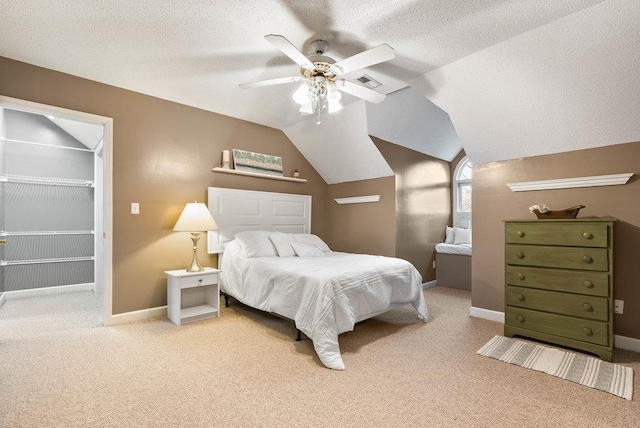 carpeted bedroom featuring ceiling fan, a spacious closet, vaulted ceiling, and a textured ceiling