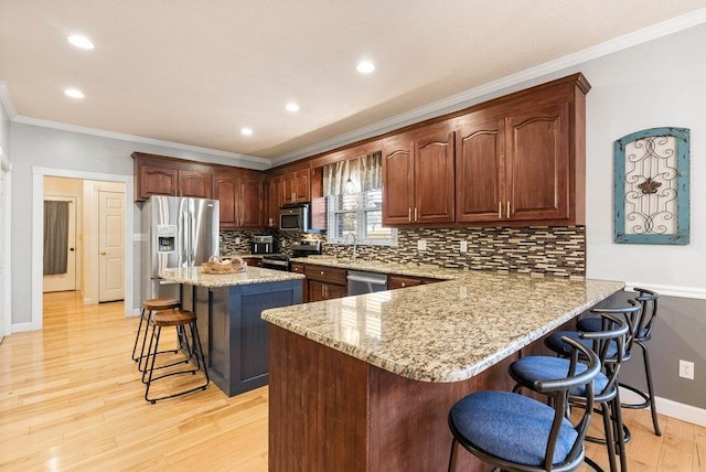 kitchen featuring a breakfast bar area, kitchen peninsula, a kitchen island, stainless steel appliances, and light stone countertops