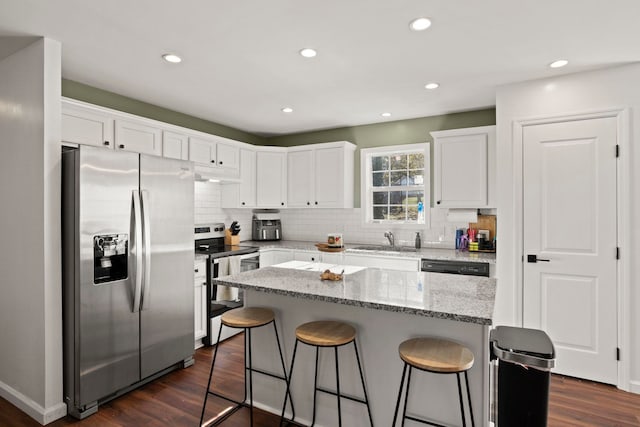 kitchen with light stone counters, stainless steel appliances, a center island, and white cabinets