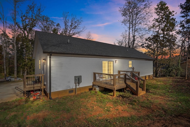 back house at dusk featuring a wooden deck and a yard