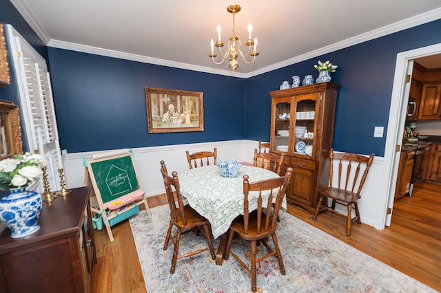 dining space featuring ornamental molding, a notable chandelier, and light hardwood / wood-style flooring