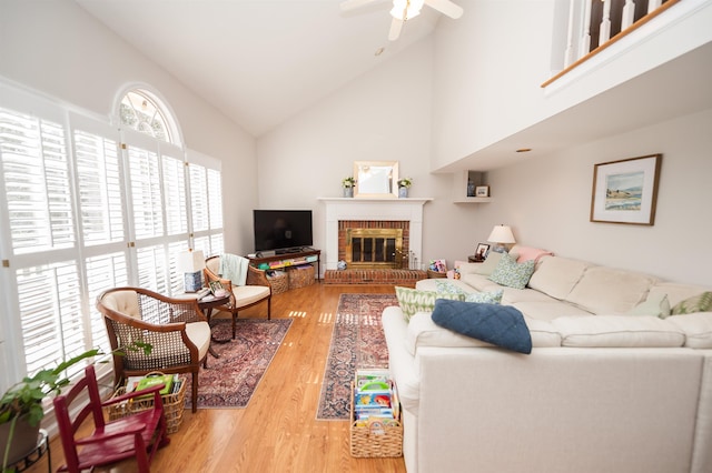 living room featuring high vaulted ceiling, a fireplace, light hardwood / wood-style floors, and ceiling fan