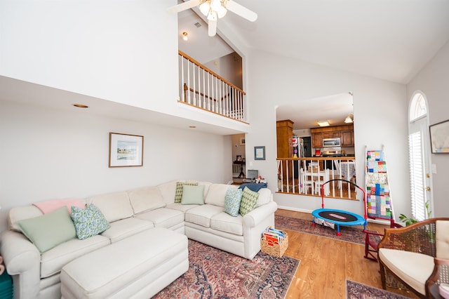 living room with ceiling fan, high vaulted ceiling, and light hardwood / wood-style floors