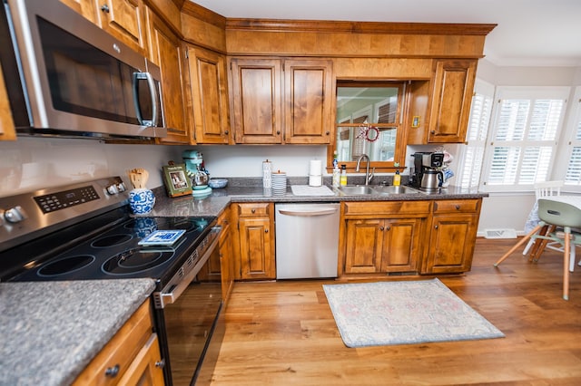 kitchen with sink, dark stone countertops, ornamental molding, stainless steel appliances, and light hardwood / wood-style floors