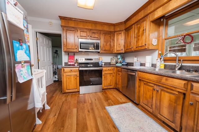 kitchen featuring sink, light wood-type flooring, ornamental molding, and appliances with stainless steel finishes