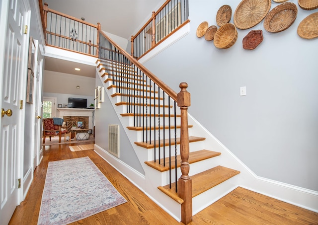 stairs featuring a fireplace, wood-type flooring, and a high ceiling