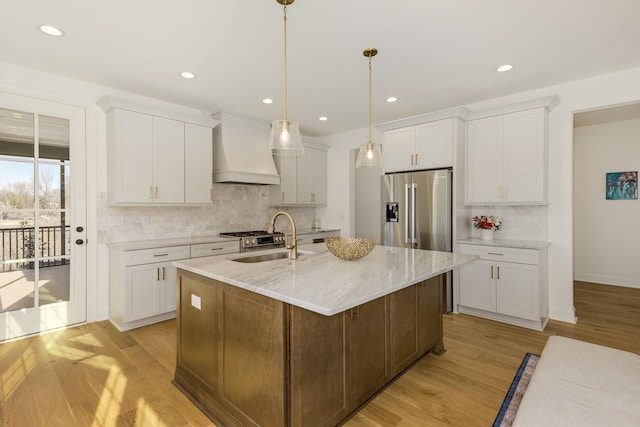 kitchen featuring high quality fridge, white cabinets, hanging light fixtures, a kitchen island with sink, and custom range hood