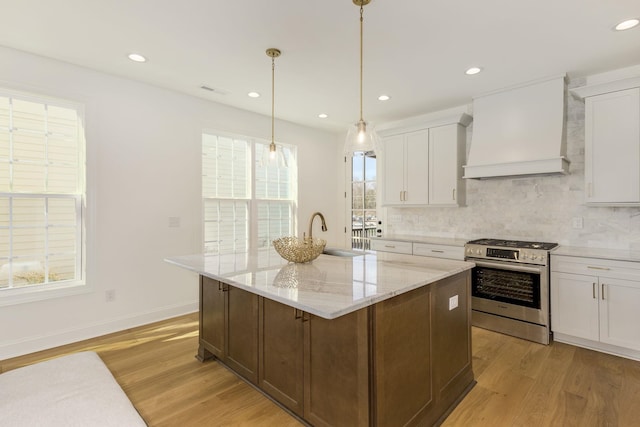 kitchen featuring premium range hood, white cabinetry, stainless steel range with gas stovetop, and an island with sink