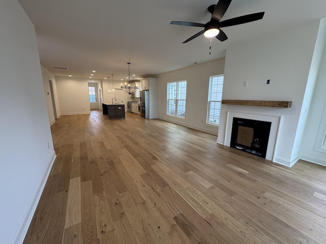 unfurnished living room with a wealth of natural light, ceiling fan with notable chandelier, and light wood-type flooring