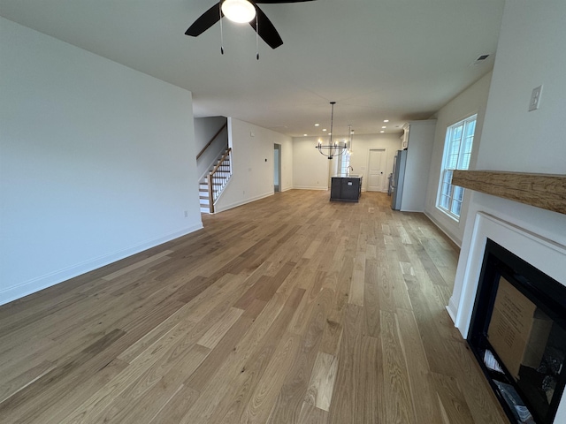 unfurnished living room featuring ceiling fan with notable chandelier and light hardwood / wood-style flooring