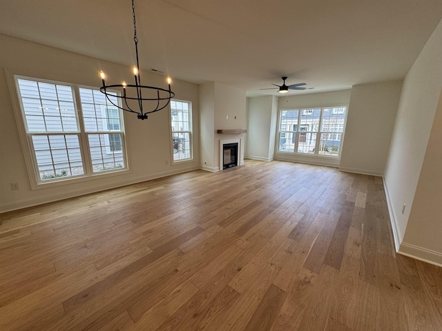 unfurnished living room featuring ceiling fan with notable chandelier and light wood-type flooring