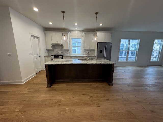 kitchen featuring sink, light wood-type flooring, appliances with stainless steel finishes, a kitchen island with sink, and white cabinets