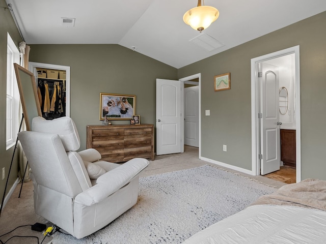 bedroom featuring vaulted ceiling, light carpet, ensuite bathroom, and a closet