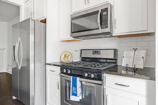 kitchen featuring decorative backsplash, stainless steel appliances, dark stone counters, and white cabinets