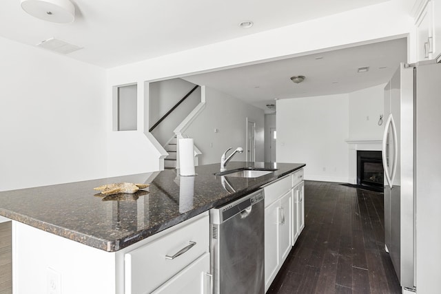 kitchen with appliances with stainless steel finishes, white cabinetry, sink, dark wood-type flooring, and a center island with sink