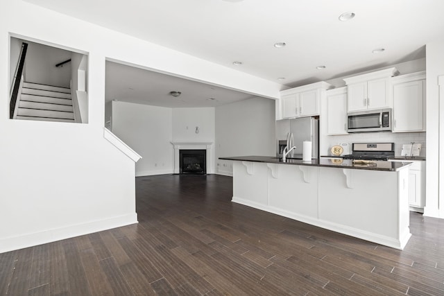 kitchen featuring a breakfast bar, a center island with sink, appliances with stainless steel finishes, dark hardwood / wood-style floors, and white cabinets