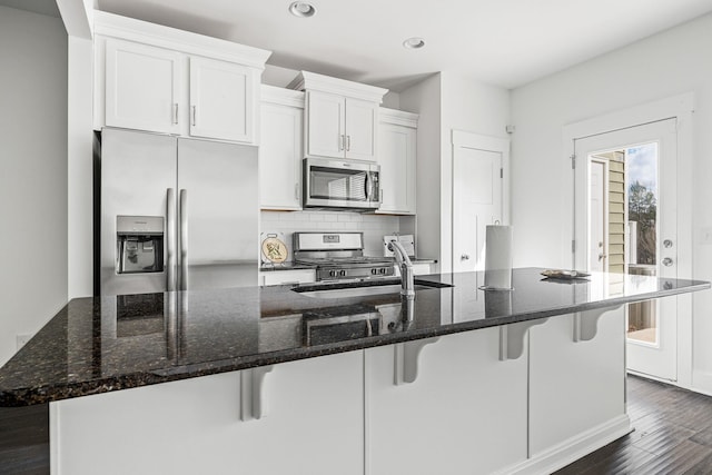 kitchen with a spacious island, appliances with stainless steel finishes, white cabinets, and dark stone counters