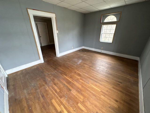 empty room with dark wood-type flooring and a drop ceiling