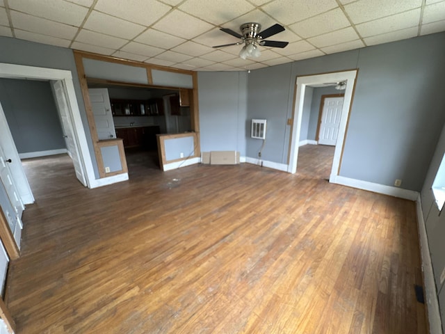 unfurnished living room with a drop ceiling, dark hardwood / wood-style flooring, heating unit, and ceiling fan