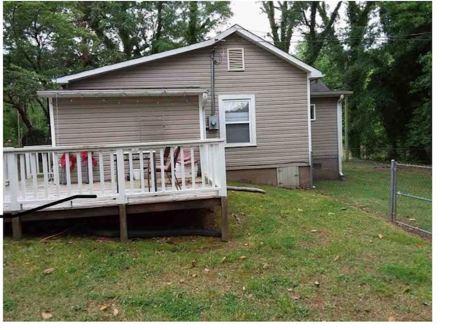 rear view of property featuring a wooden deck and a lawn