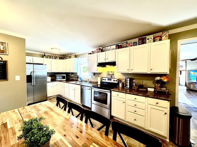 kitchen with appliances with stainless steel finishes, white cabinetry, sink, ornamental molding, and light hardwood / wood-style floors