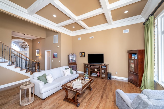 living room featuring an inviting chandelier, ornamental molding, coffered ceiling, and light hardwood / wood-style floors