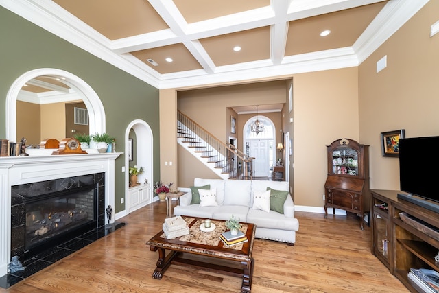 living room featuring coffered ceiling, a fireplace, crown molding, and light hardwood / wood-style flooring