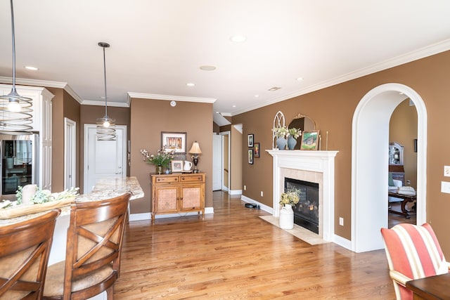 interior space with a tiled fireplace, hanging light fixtures, ornamental molding, and light wood-type flooring