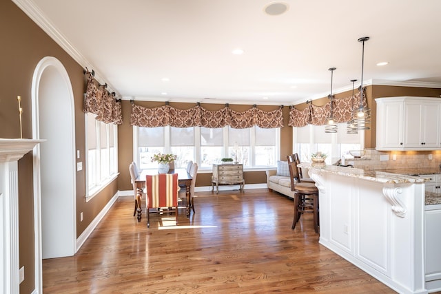 kitchen with hardwood / wood-style flooring, a breakfast bar area, crown molding, light stone counters, and white cabinets