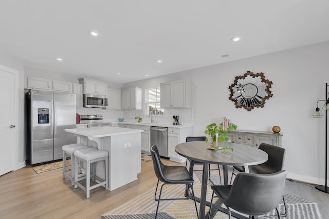 kitchen featuring white cabinetry, backsplash, stainless steel appliances, a kitchen island, and light wood-type flooring