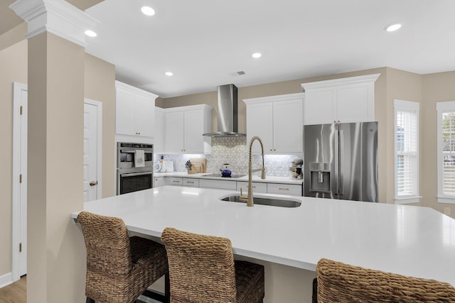 kitchen with white cabinetry, appliances with stainless steel finishes, sink, and wall chimney range hood