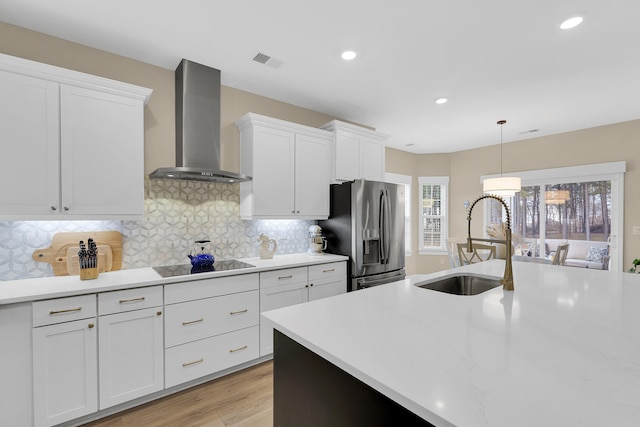 kitchen featuring stainless steel refrigerator with ice dispenser, wall chimney exhaust hood, sink, and white cabinets