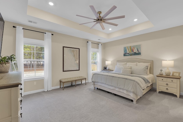 bedroom with a raised ceiling, light carpet, and ceiling fan